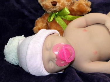 Full Silicone Doll baby doll lies on a vibrant purple blanket, accompanied by a charming teddy bear, evoking a sense of comfort and joy.